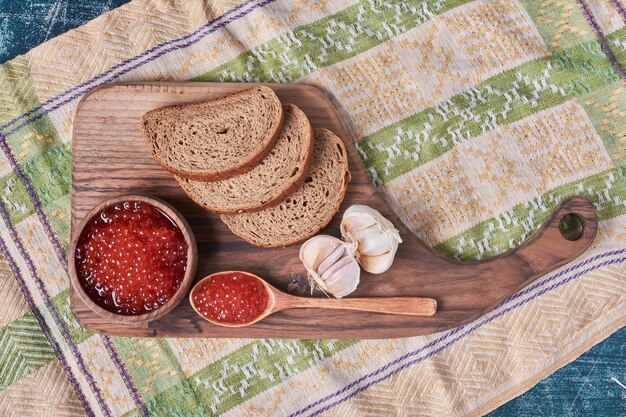 Caviar rojo sobre tabla de madera con pan.