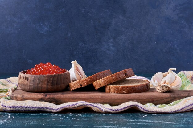 Caviar rojo sobre tabla de madera con rebanadas de pan.