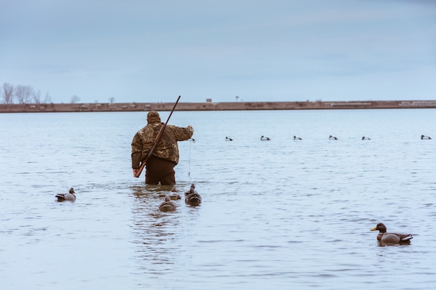 Cazador con un rifle en la espalda tomando un descanso de la caza y la captura de un pez en el lago con patos