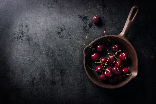 Cazo con cerezas sobre una mesa de madera negra visto desde arriba