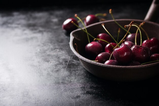 Cazo con cerezas sobre una mesa de madera negra