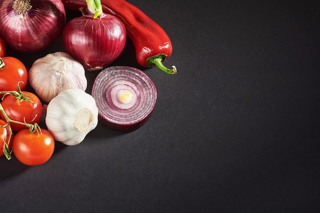 Cebolla y ajo y pimientos picantes y tomates aislados en un negro.