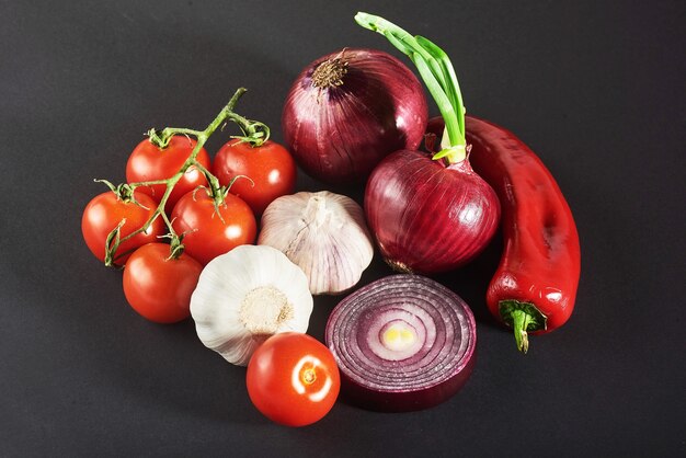 Cebolla y ajo y pimientos picantes y tomates aislados en un negro.