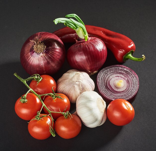 Cebolla y ajo y pimientos picantes y tomates aislados en un negro.