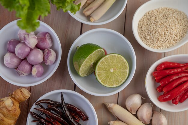 Cebollas rojas, limón, hierba de limón, chiles, ajo, galanga y lechuga en una taza sobre un piso de madera.