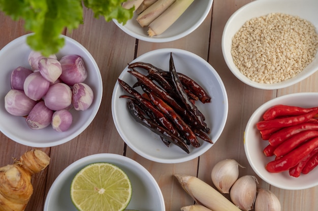 Foto gratuita cebollas rojas, limón, hierba de limón, chiles, ajo, galanga y lechuga en una taza sobre un piso de madera.