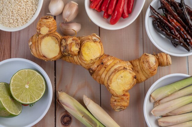 Cebollas rojas, limón, hierba de limón, chiles, ajo, galanga y lechuga en una taza sobre un piso de madera.