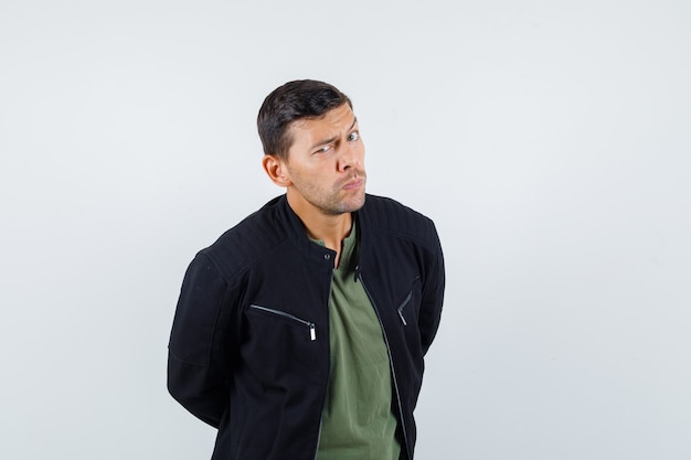 Ceja frunciendo el ceño masculino joven en camiseta, chaqueta y aspecto dudoso. vista frontal.