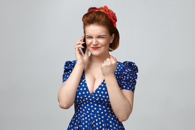 Celebración, éxito y victoria. Chica pin up exitosa alegre en elegante traje retro con conversación telefónica en estudio con móvil,