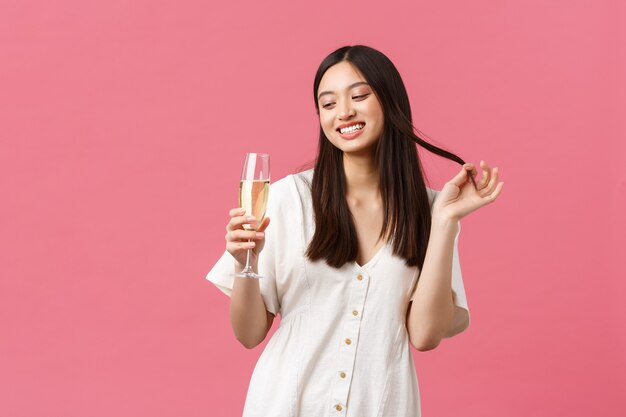 Celebración, fiestas y concepto de diversión. Mujer joven coqueta y coqueta con copa de champán tratando de seducir al chico en la celebración del evento, riendo y sonriendo tontamente sobre fondo rosa.