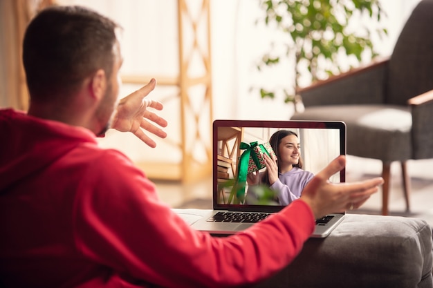 Celebración y vacaciones durante el concepto de cuarentena. Amigos o familiares desempacando regalos mientras hablan mediante videollamada. Luce feliz, alegre, sincera. Concepto de año nuevo, tecnologías, emociones.