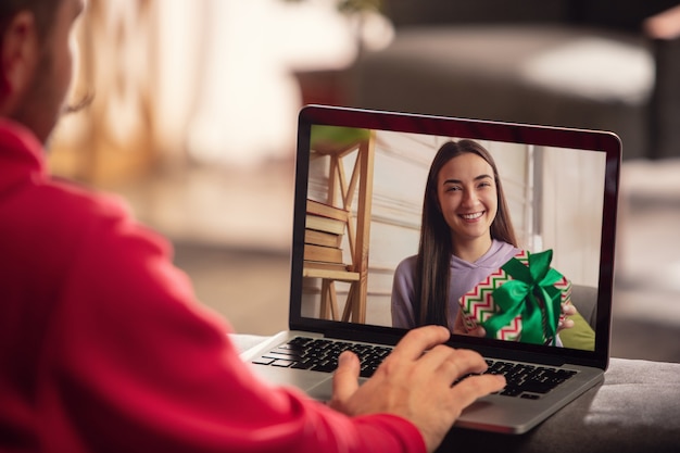 Celebración y vacaciones durante el concepto de cuarentena. Amigos o familiares desempacando regalos mientras hablan mediante videollamada. Luce feliz, alegre, sincera. Concepto de año nuevo, tecnologías, emociones.