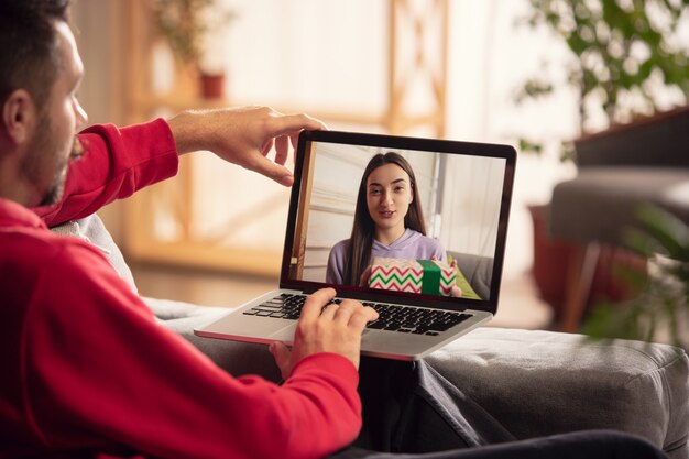 Celebración y vacaciones durante el concepto de cuarentena. Amigos o familiares desempacando regalos mientras hablan mediante videollamada. Luce feliz, alegre, sincera. Concepto de año nuevo, tecnologías, emociones.