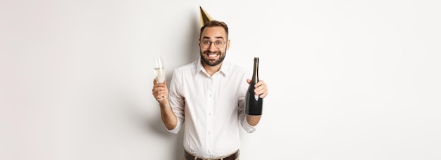 Celebración y vacaciones feliz cumpleaños chico disfrutando de la fiesta de cumpleaños con un divertido sombrero de cono y bebiendo