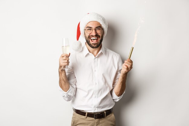 Celebración y vacaciones de invierno. Hombre guapo con barba que tiene fiesta de año nuevo, con destellos de fuegos artificiales y champán, con sombrero de santa