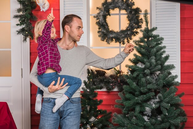 Celebraciones de navidad con hombre y niña al lado de árbol de navidad