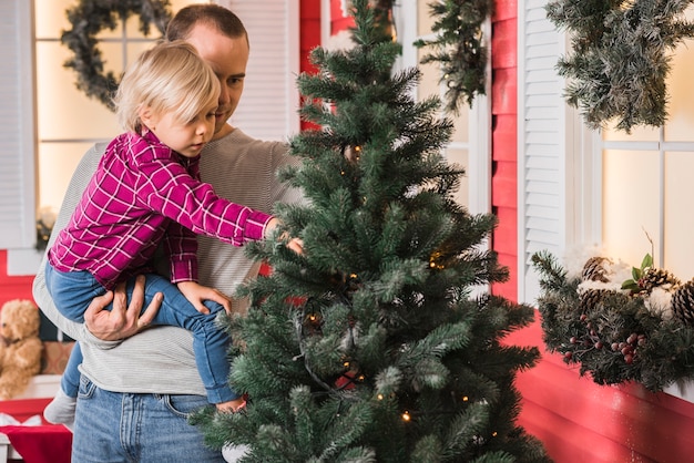 Celebraciones de navidad con padre e hija decorando árbol de navidad