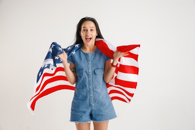 Celebrando un día de la Independencia. Estrellas y rayas. Mujer joven con la bandera de los Estados Unidos de América aislado en la pared blanca del estudio. Parece loca, feliz y orgullosa como una patriota de su país.