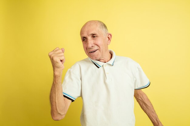 Celebrando la victoria. Retrato de hombre mayor caucásico aislado sobre fondo amarillo de estudio. Hermoso modelo emocional masculino. Concepto de emociones humanas, expresión facial, ventas, bienestar, publicidad. Copyspace.