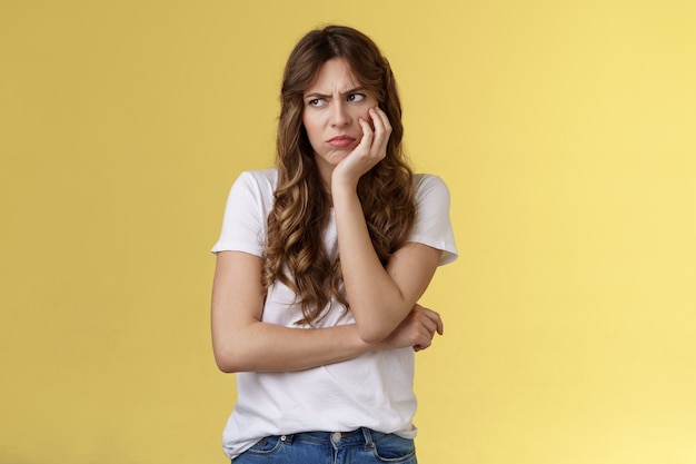 Celos malestar enojado novia temperamental magra palma sonriendo burlona fruncir el ceño molesto mirada sombría a un lado girar a la izquierda consternación sentado solo ofendido pensamiento excesivo reina del drama soporte fondo amarillo.