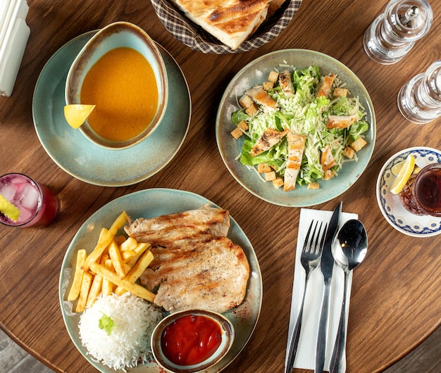 Cena con ensalada César, sopa de lentejas y filete de pollo servido con arroz y papas fritas.