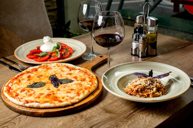 Cena con pizza margherita, ensalada, pasta y vino.