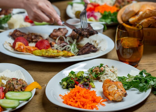 Cena en platos blancos que contienen carne y verduras, bocadillos.