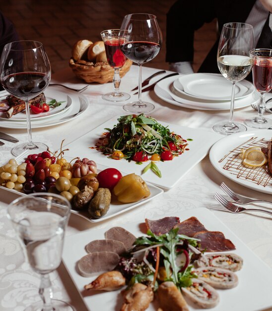 cena preparada con vino tinto, plato de pepinillos, plato de carne, ensalada fresca