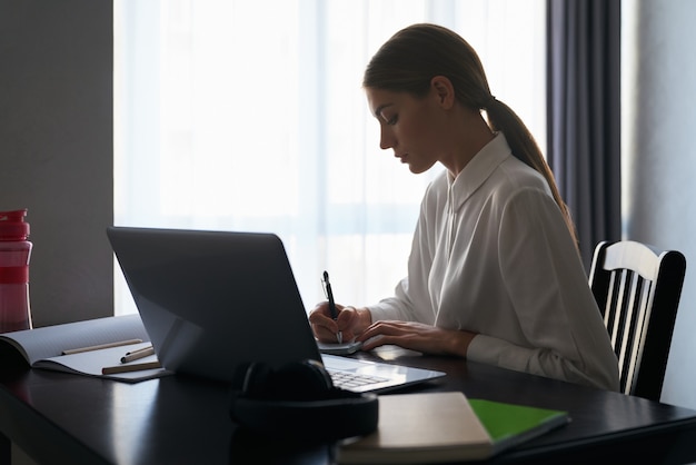 Centrado mujer sentada a la mesa y trabajando en equipo portátil