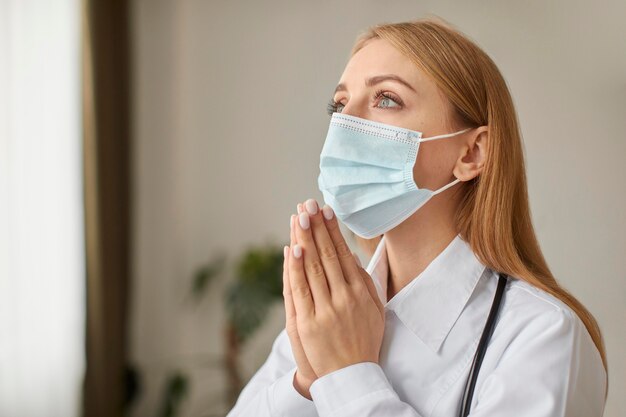 Centro de recuperación de Covid doctora con estetoscopio y máscara médica rezando