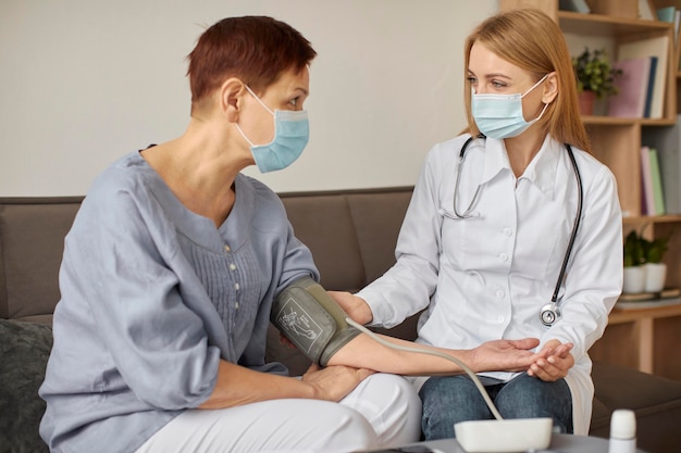 Centro de recuperación de covid doctora con máscara médica que controla la presión arterial del paciente anciano