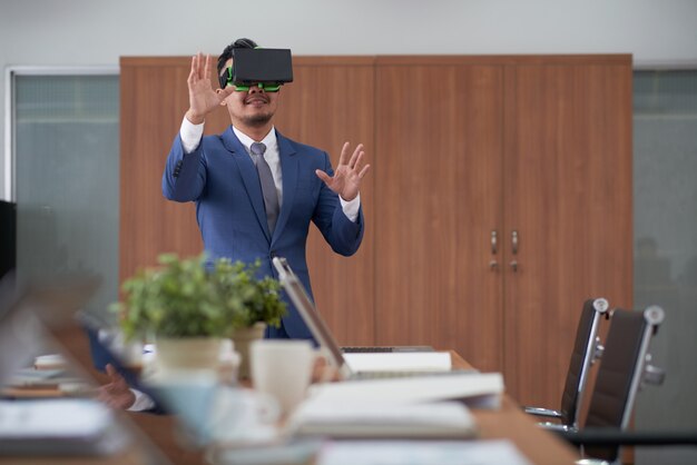 CEO asiático en traje usando casco de realidad virtual en la sala de juntas