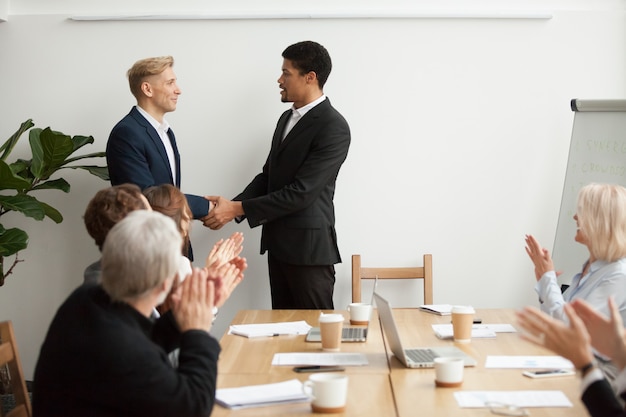 CEO negro y hombre de negocios blanco dándose la mano en la reunión del grupo