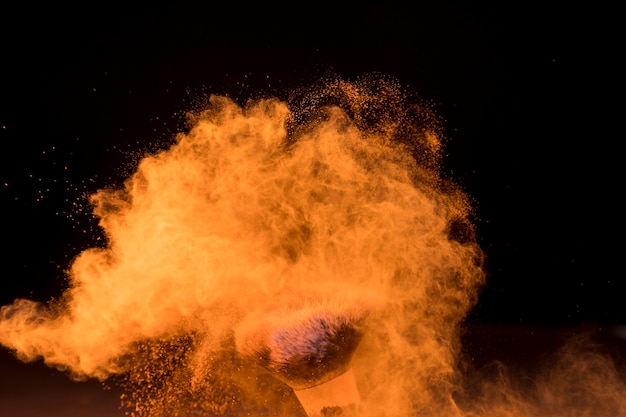 Cepillo cosmético en la nube de polvo de maquillaje sobre fondo oscuro