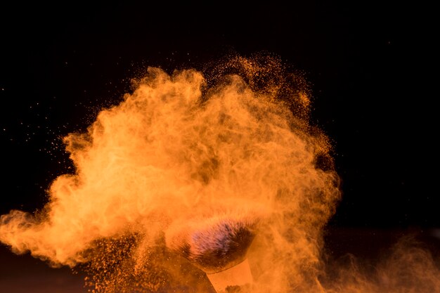 Cepillo cosmético en la nube de polvo de maquillaje sobre fondo oscuro