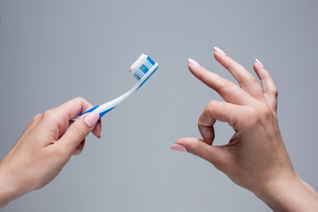 Cepillo de dientes en manos de mujer en gris