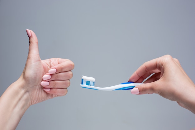 Cepillo de dientes en manos de mujer en gris