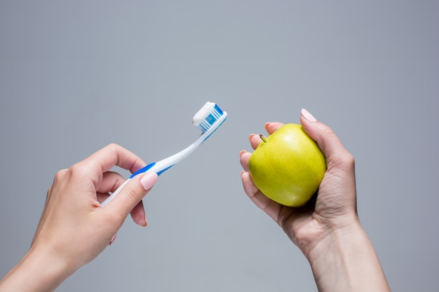 Cepillo de dientes y manzana en manos de mujer en gris