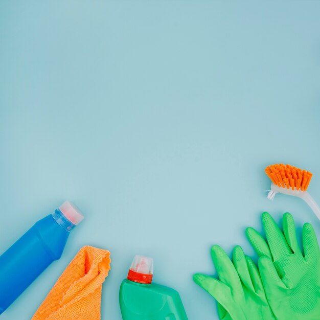 Cepillo; guantes verdes Servilleta y botella sobre fondo azul
