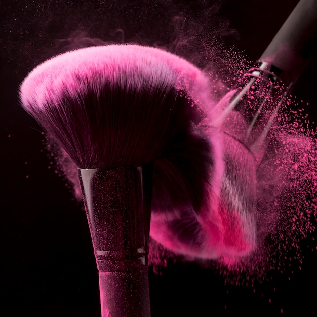 Cepillos coloretes que dispersan el polvo de color rosa sobre fondo negro