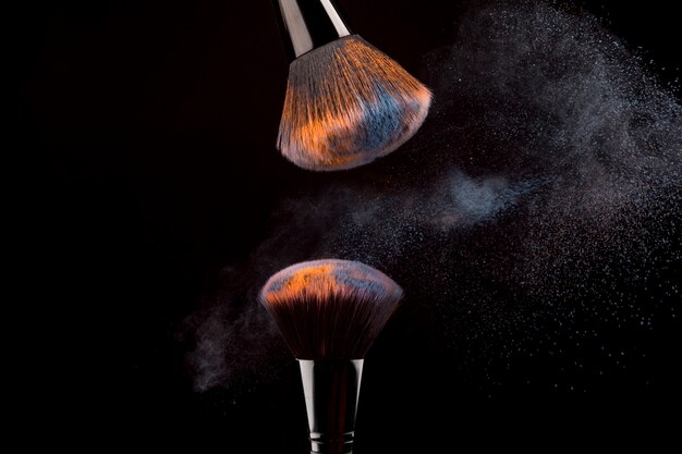 Cepillos cosméticos con niebla de polvo sobre fondo oscuro