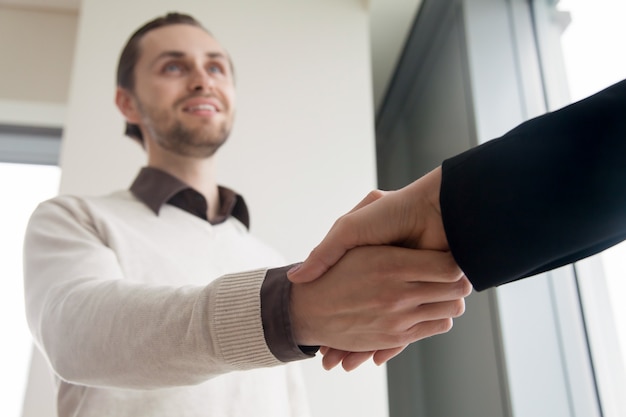 Cerca de apretón de manos, sonriente hombre de negocios y cliente estrechándole la mano