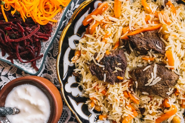 Cerca de arroz con zanahorias adornadas con trozos de cordero servidos con pepinillos y yogurt