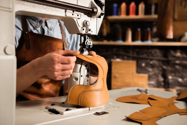 Cerca de un artesano masculino cosiendo piezas de cuero