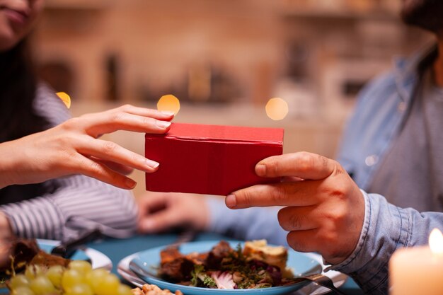 Cerca de la caja de regalo celebrada por marido y mujer durante una cena romántica