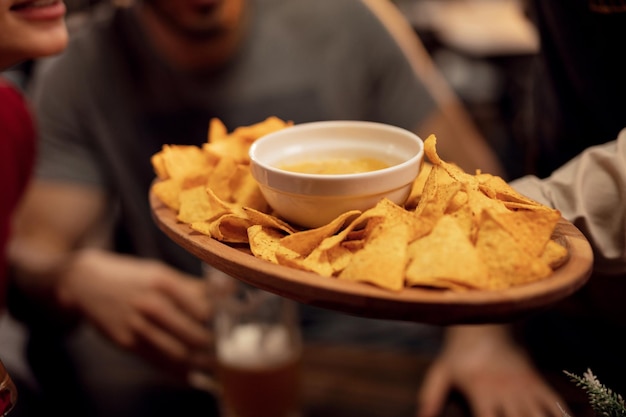 Cerca de camarero sirviendo chips de tortilla con salsa de salsa a los invitados en un pub