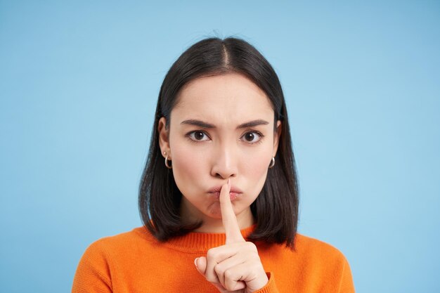 Cerca de la chica asiática morena enojada shush toca los labios con el dedo le dice que se calle sobre b