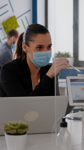 Cerca de compañeros de trabajo con mascarilla trabajando juntos en el proyecto financiero usando tableta ...