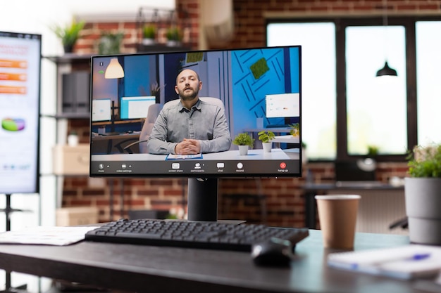 Cerca de la conversación de videollamada con un colega en el monitor en la oficina de negocios vacía. Videoconferencia remota en la computadora para tener una reunión de teleconferencia en línea con el hombre en el espacio de trabajo.