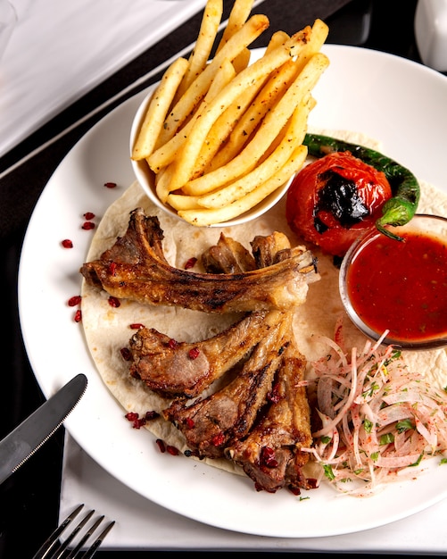 Cerca de costillas de cordero kebab papas fritas cebolla y hierbas mezcla salsa de tomate y verduras a la parrilla